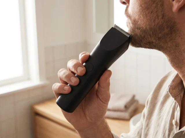 Man trimming his beard with a cordless trimmer in a bright bathroom