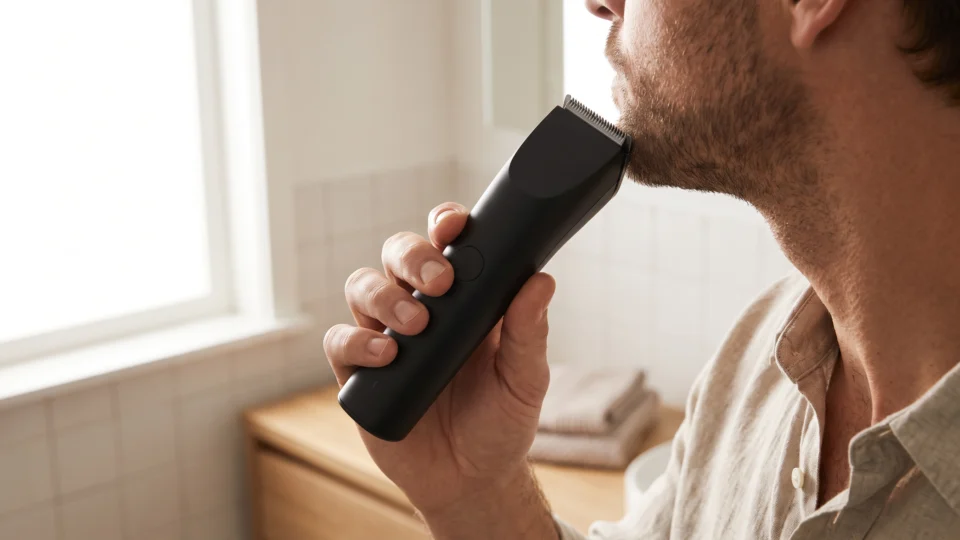Man trimming his beard with a cordless trimmer in a bright bathroom